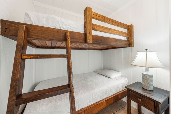 A bunk bed with a wooden frame, a white mattress, and a bedside table with a lamp.