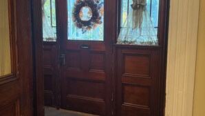 Une porte d’entrée en bois, dotée d’un panneau de verre et ornée d’une guirlande, qui donne sur un intérieur recouvert de moquette.