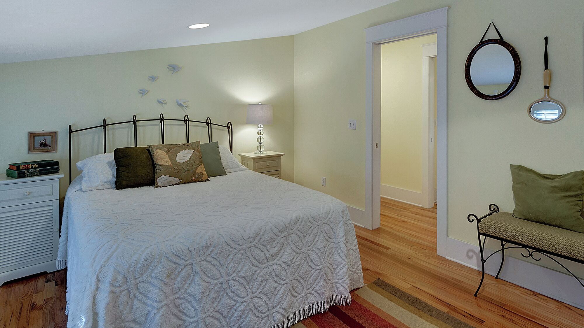 Un dormitorio con cama, mesita de noche, lámpara y un espejo en la pared.