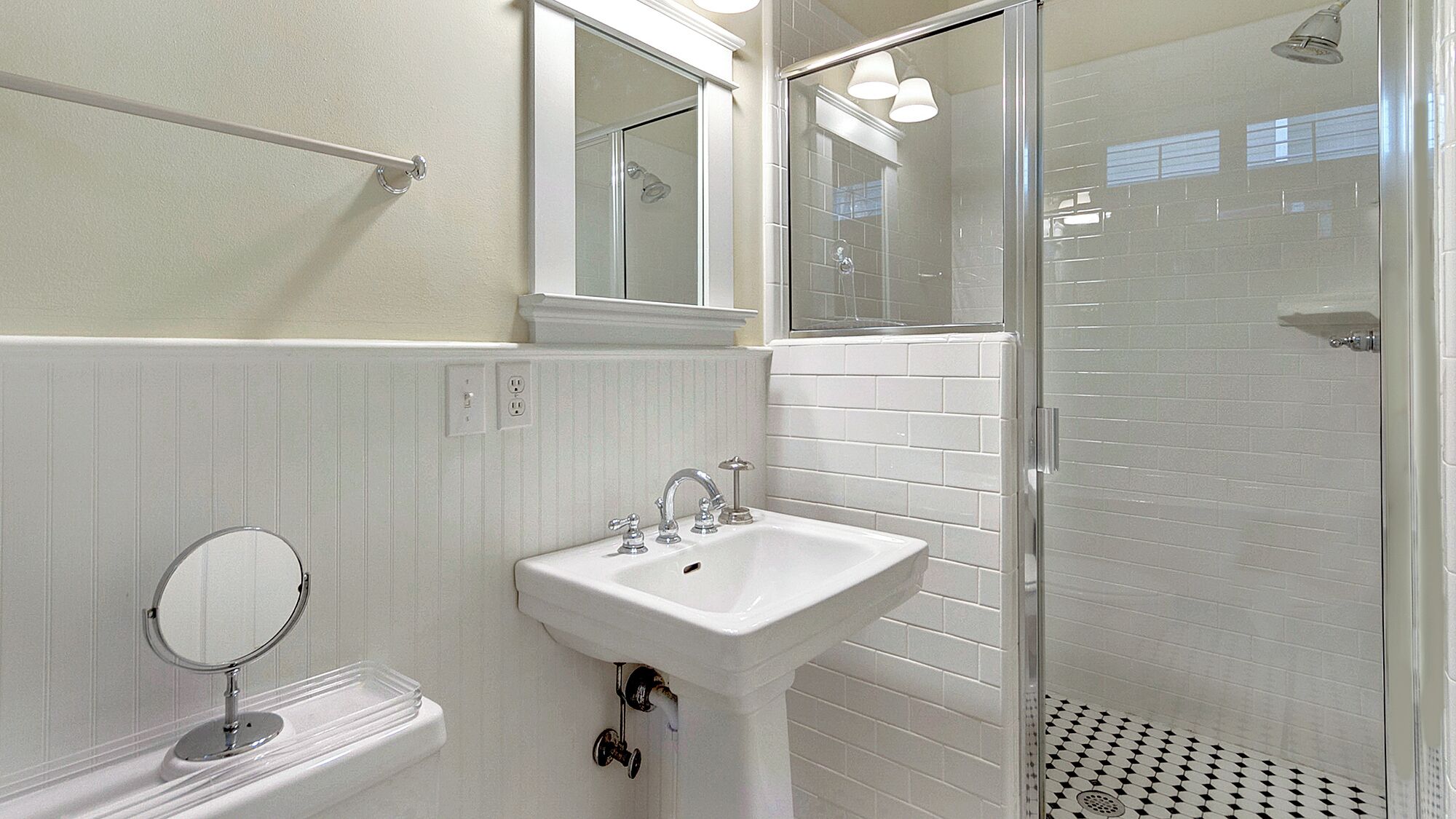 A bathroom with a white sink, a mirror, a glass shower enclosure, and a tiled shower floor.