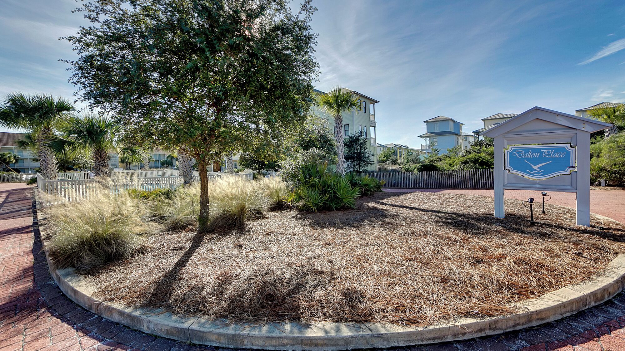 A landscaped area with a sign reading "Valon Place," surrounded by a white fence, trees, and a mulched ground.