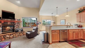 A spacious living area with a stone fireplace, a comfortable leather chair, and a television mounted above it. - Cozy Mountain Retreat (Dillon)