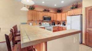 A kitchen with wooden cabinets, a stainless steel microwave, a white refrigerator, and a tiled island. - Cozy Mountain Retreat (Dillon)