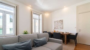 Een moderne woonkamer met een grijze bank, een eettafel met stoelen, en een groot raam.
