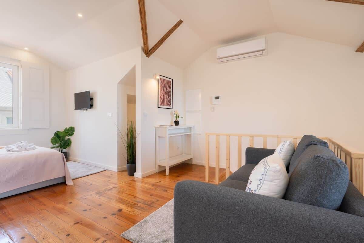 Une chambre à coucher moderne avec un lit, un canapé gris, une console blanche et un escalier en bois.