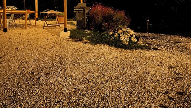 Un quiosco con luces colgantes, una mesa y sillas bajo un cielo nocturno con luna visible.