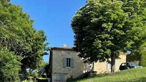 Un edificio de piedra con una pequeña ventana y contraventanas, rodeado de césped verde y exuberantes árboles.