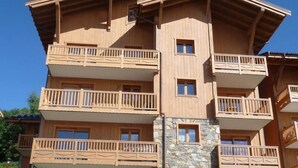 Un immeuble en bois à plusieurs étages, doté de balcons et agrémenté d’éléments en pierre, se dressant sous un ciel d’un bleu limpide.