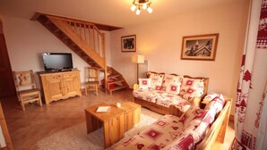 Un salon chaleureux avec un escalier en bois, un canapé agrémenté de coussins à motifs, un téléviseur posé sur un meuble en bois et un tapis moelleux.
