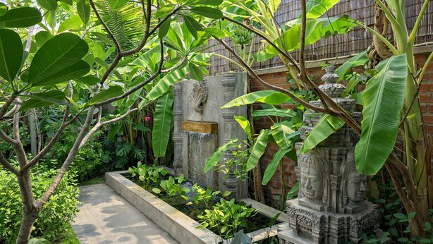 Un jardín con estatuas de piedra, un sendero de hormigón y abundante vegetación.