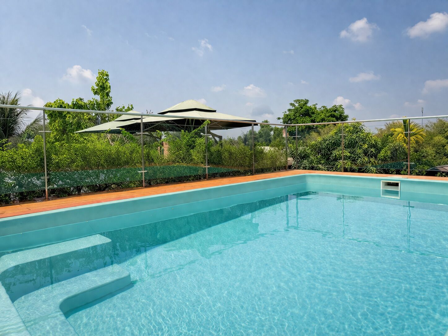 Une piscine à eau claire, dotée d’une terrasse en bois, entourée de verdure et agrémentée d’un espace abrité.