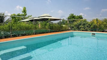 Une piscine à eau claire, dotée d’une terrasse en bois, entourée de verdure et agrémentée d’un espace abrité.
