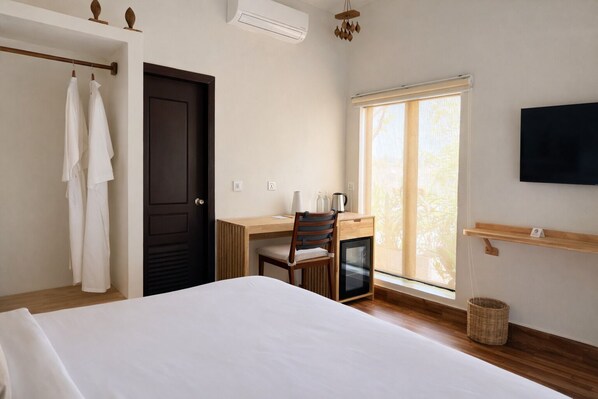 A bedroom with a bed, a desk with a chair, a TV, and a window with blinds.