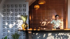 Zona de recepción con mostrador de madera, pared decorativa con patrones geométricos y lámparas colgantes de mimbre.