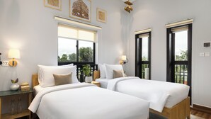 Una habitación de hotel con dos camas, una mesita de noche, una lámpara, una ventana y una puerta.