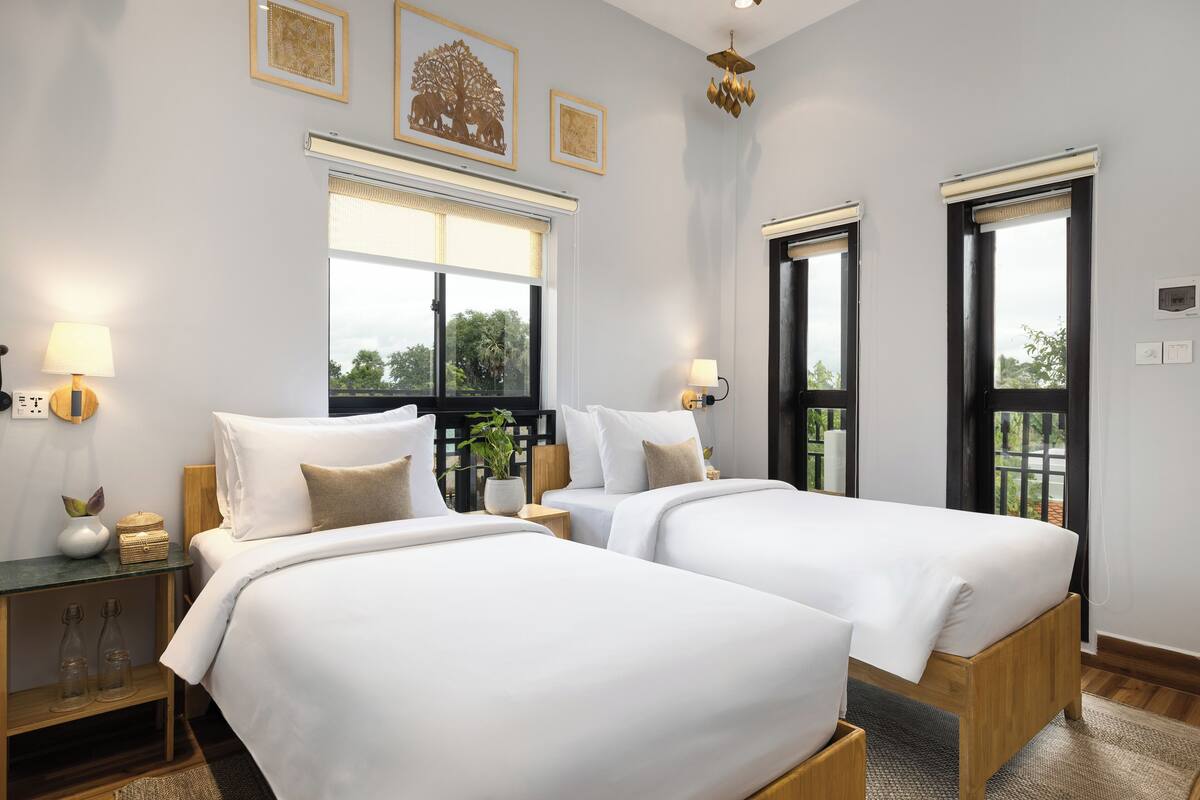 Una habitación de hotel con dos camas, una mesita de noche, una lámpara, una ventana y una puerta.