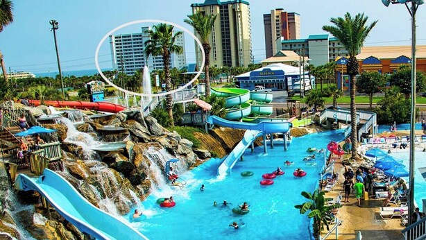 Ein Wasserpark mit mehreren Wasserrutschen und Wasserspielen, umgeben von Palmen und Gebäuden.