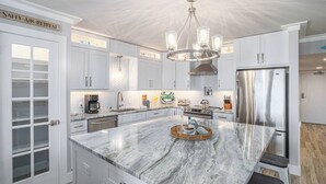 Uma cozinha moderna com armários brancos, uma ilha de mármore, eletrodomésticos de aço inoxidável e um lustre.