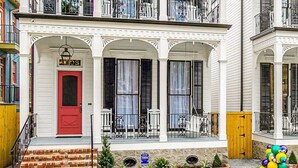 Ein zweistöckiges Gebäude mit roter Tür, weißer Verkleidung und einem Balkon mit schwarzen Geländern.