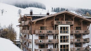 Un bâtiment en bois à plusieurs étages, doté de balcons, qui ressemble probablement à un hôtel ou à un chalet, et qui se dresse sur fond de montagnes enneigées.