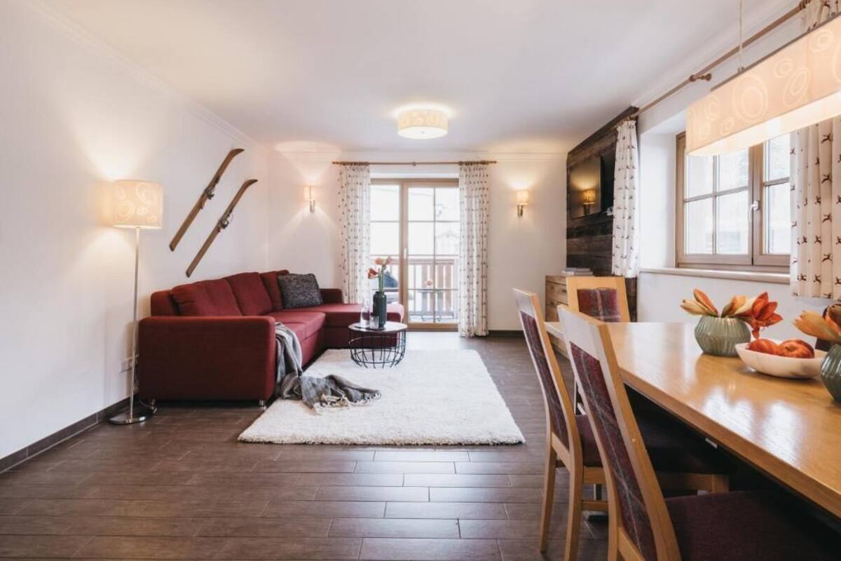 Un salon moderne avec un canapé rouge, une table à manger en bois entourée de chaises, une cheminée et une grande fenêtre agrémentée de rideaux.
