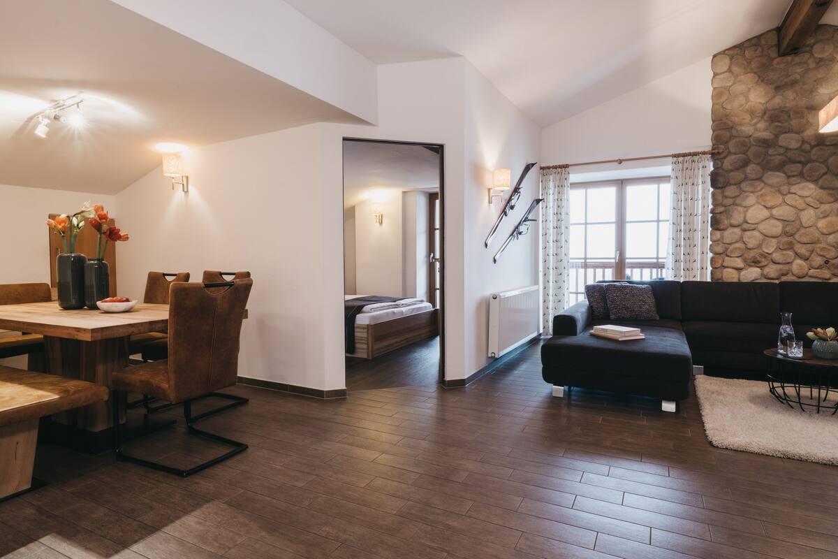 Un salon moderne avec un plancher en bois, un coin repas comprenant une table et des chaises, un canapé et un escalier menant à un niveau supérieur.