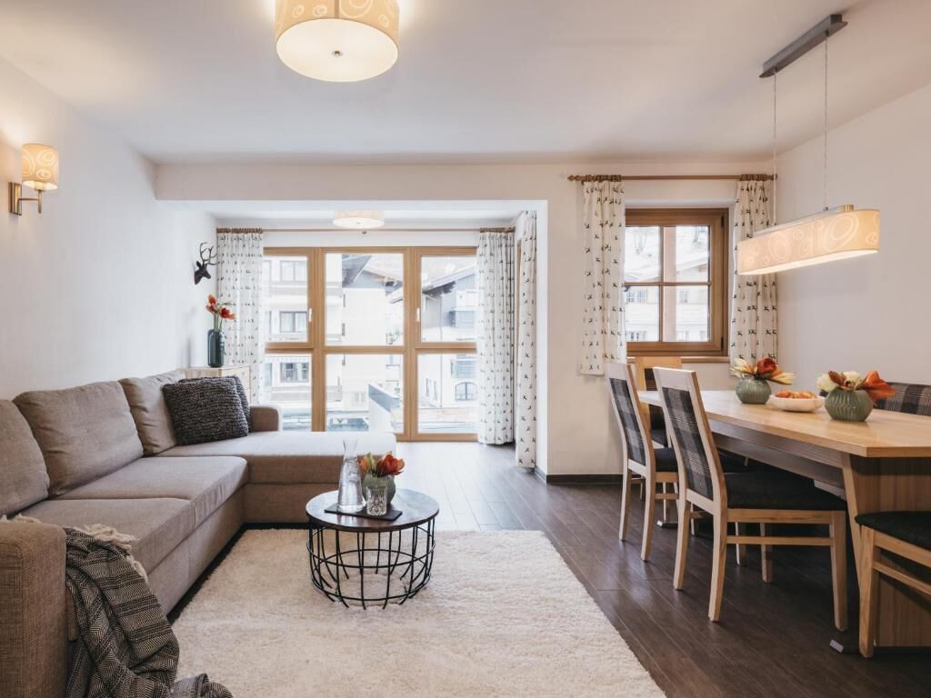 A modern living room with a sofa, a dining table with chairs, a coffee table, and a large window with curtains.