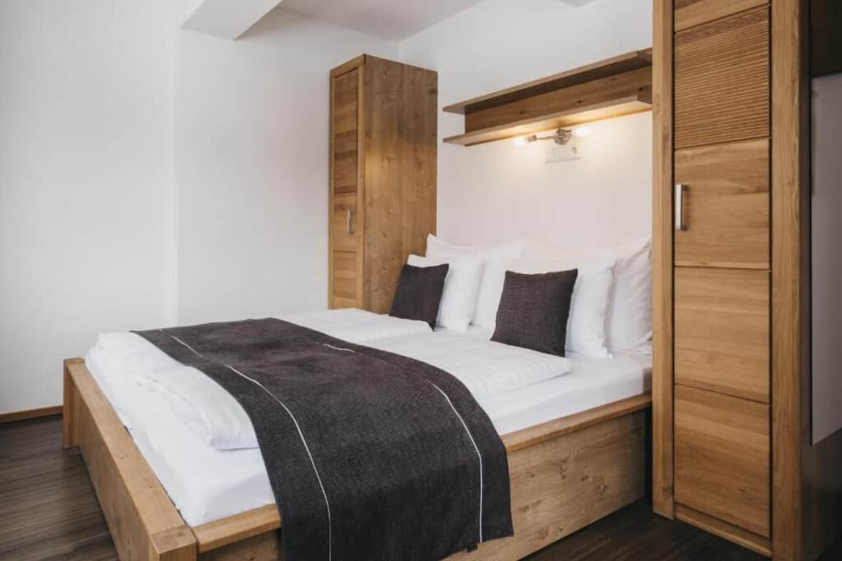 Une chambre moderne avec un lit en bois, une literie blanche et un plaid foncé.
