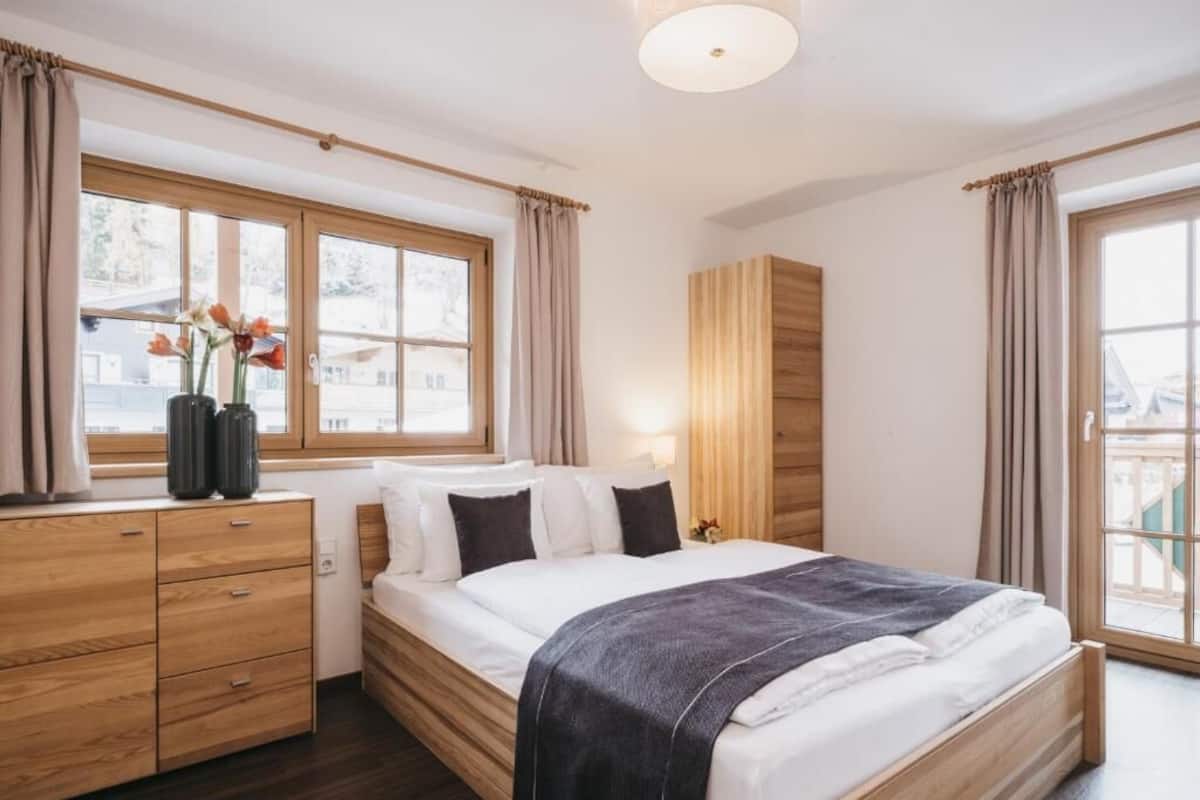 Une chambre à coucher moderne avec un lit en bois, une table de chevet, une commode et une fenêtre avec des rideaux.