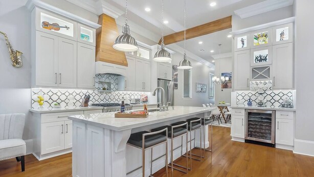 Una cocina moderna con armarios blancos, una isla grande con taburetes y luminarias colgantes, además de un horno empotrado.