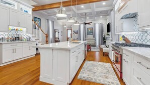 Una cocina moderna con armarios blancos, una isla central, luces colgantes y techo de madera.