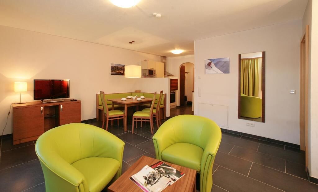 A hotel room with a dining area, a TV, and a green sofa.