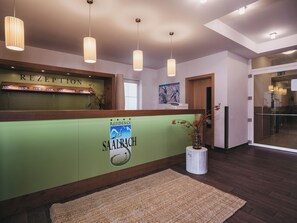 Zona de recepción con un mostrador verde, una mesa de recepción y una puerta de vidrio que da a otra sala.