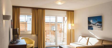 A hotel room with a sofa, armchair, and a small table. There is a window with curtains, a door leading outside, and a painting on the wall.
