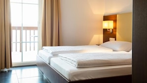 Une chambre d’hôtel avec deux lits, une porte-fenêtre coulissante donnant sur le balcon et une lampe de chevet.