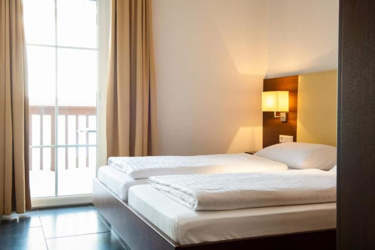 Une chambre d’hôtel avec deux lits, une porte-fenêtre coulissante donnant sur le balcon et une lampe de chevet.