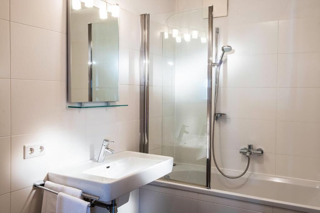 A modern bathroom with a glass shower enclosure, a white sink, and a mirror above it.