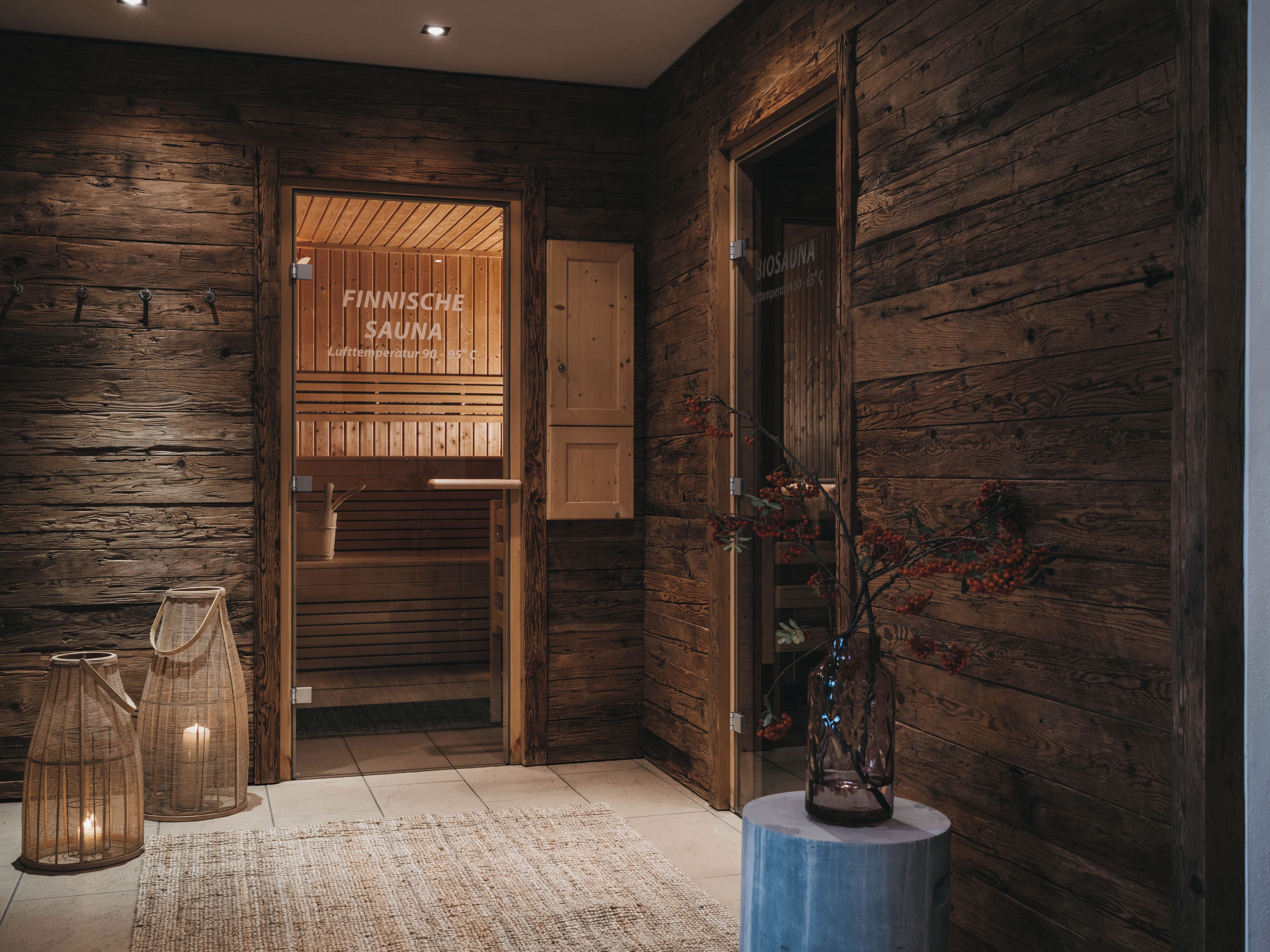 A wooden interior with a sauna sign, a glass door, and a vase with branches.