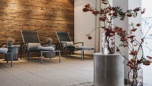 Un espace d’attente moderne avec des murs recouverts de panneaux en bois, deux fauteuils confortables, une petite table ornée d’un vase de fleurs et une grande fenêtre avec des rideaux.