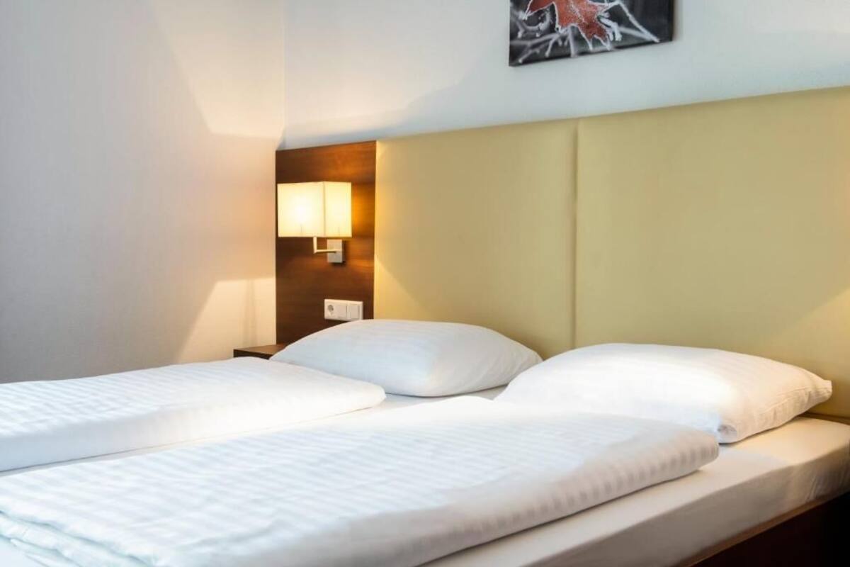Une chambre d’hôtel avec un lit, une table de chevet, une lampe fixée au mur et un tableau accroché au mur.