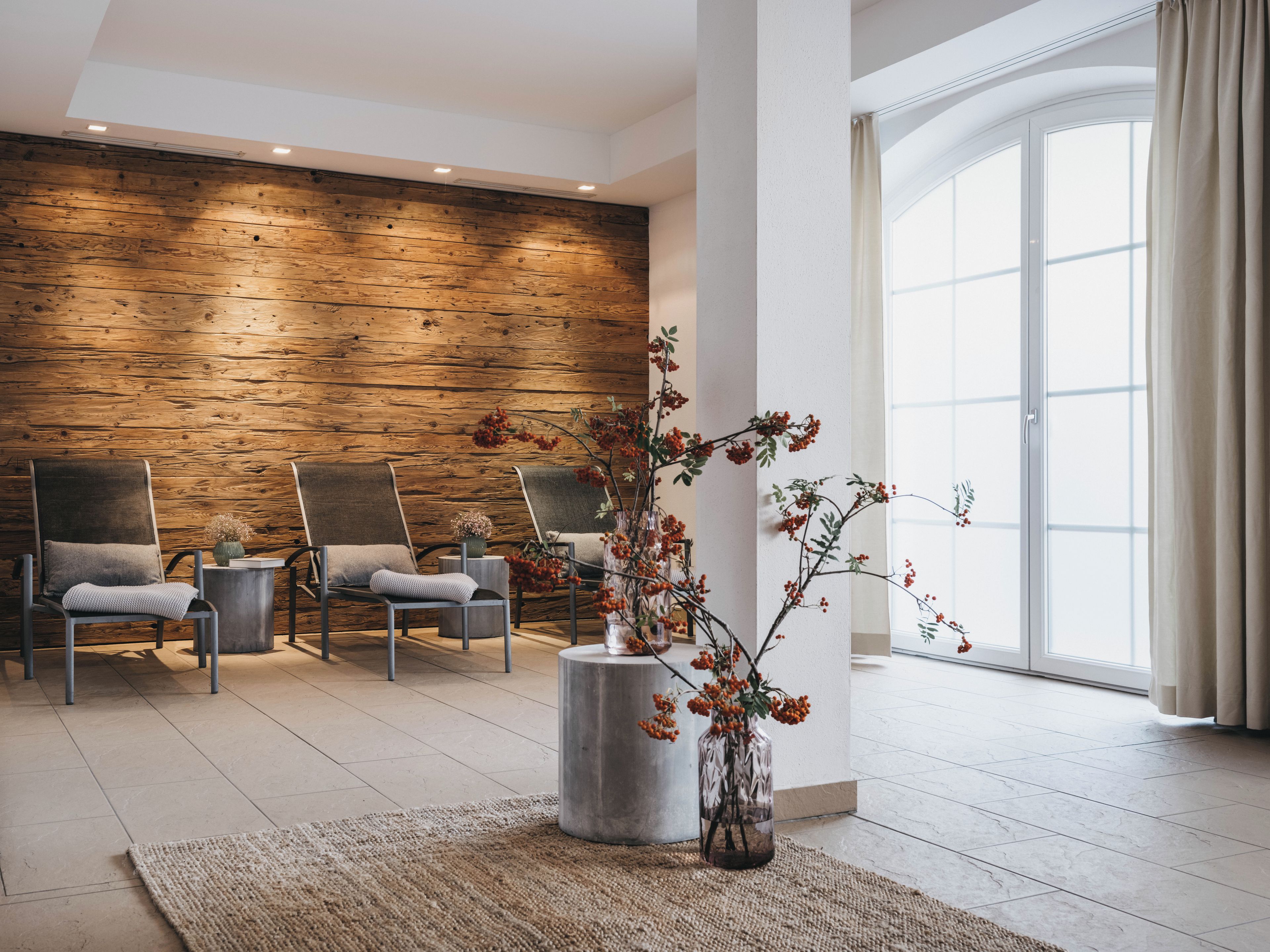 A modern interior with a wooden wall, two armchairs, a round table, and a vase with branches.