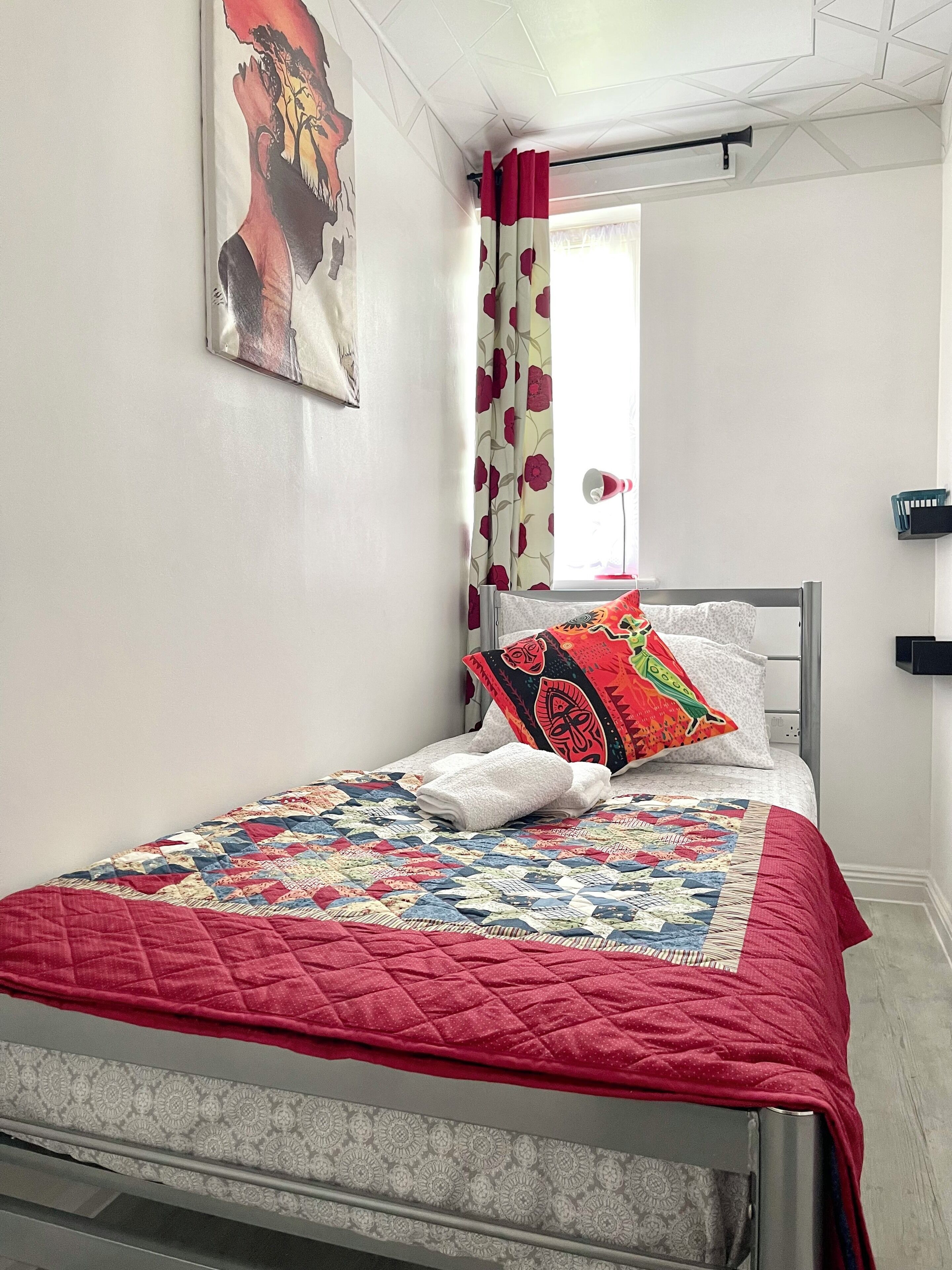 Una cama bien hecha con un edredón rojo, una almohada colorida y una toalla blanca.