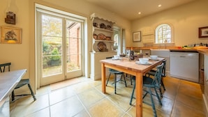 Une cuisine avec une table et des chaises en bois, une étagère intégrée où sont rangés la vaisselle, et une fenêtre donnant sur l’extérieur.