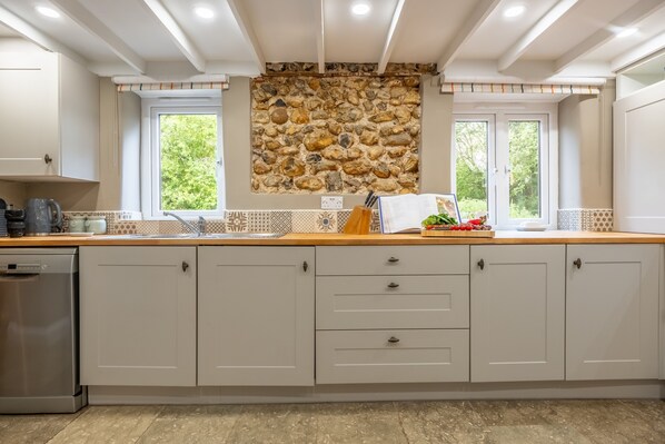 A modern kitchen with white cabinets, a stone backsplash, and a window providing natural light.