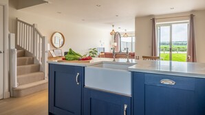 A modern kitchen with a central island, a dining area with a view, and a staircase leading to another level. - Kingfishers Cove, Titchwell, Norfolk (Wells-next-the-Sea)