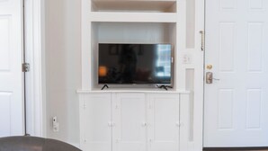 A white entertainment unit with a flat-screen TV mounted above it, a white door to the right, and a white wall. - Cute & Compact 1BR - Easy Walk to Town (St. Augustine)