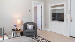 A hotel room with a bed, a chair, a TV mounted on a cabinet, and a lamp on a side table. - Cute & Compact 1BR - Easy Walk to Town (St. Augustine)