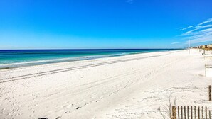 Ein weiter Sandstrand mit klarem, blauem Wasser und strahlend blauem Himmel.
