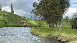 A river flowing through a grassy landscape with trees and rocks. - River House to Relax, Rejuvenate, and connect with the quietness of nature. (Saint Ignatius)