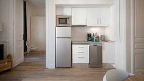 Una cocina compacta con armarios blancos, un refrigerador de acero inoxidable, un microondas, un lavavajillas y una cafetera.
